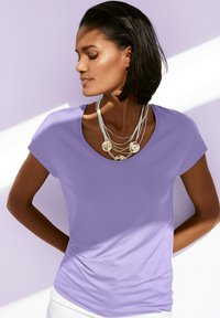 Paarse t-shirt met een bootcut halslijn en korte mouwen, gemaakt van zacht materiaal. Gelaagde zilveren ketting met ronde accenten.