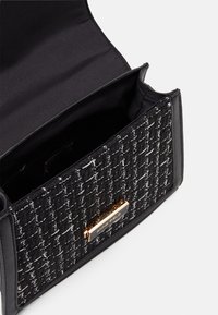 Svart handväska med ett strukturerat tyg i vävt mönster, guldfärgade detaljer och ett foder av tyg på insidan. Stängs med lock.
