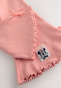 Pink ribbed fabric featuring a scalloped hem, with a tag displaying a character design and a bow accent on the top.