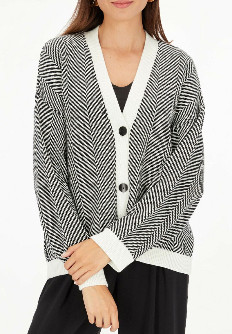 Czarny i biały kardigan w jodełkę z dekoltem w serek, dwiema dużymi czarnymi guzikami i białymi mankietami, wykonany z miękkiej, teksturowanej dzianiny.