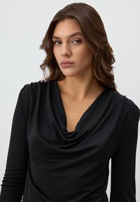 Zwarte, lange mouwen top met een colnek, gemaakt van glad, elastisch materiaal en subtiele drapering. Geen zichtbare patronen of hardware.