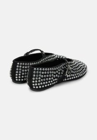 Zapatos negros sin cordones con una superficie texturizada, tachuelas plateadas, forma redondeada y una correa con hebilla en el empeine.