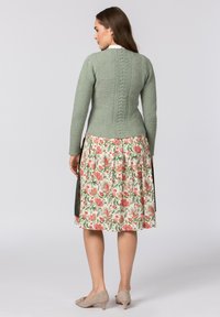 Grün gestrickter Pullover mit strukturiertem Rücken, kombiniert mit einem rock im Blumenmuster in Creme, Rot und Grün. Helle graue Schuhe runden das Outfit ab.