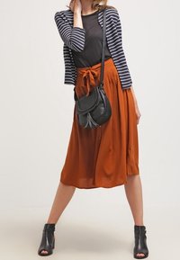 Black T-shirt, navy striped cardigan, rust-colored wrap skirt, and black ankle boots. Black crossbody bag with tassel detail.