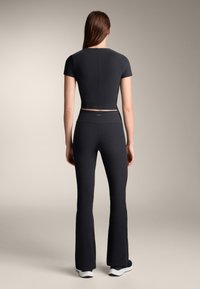 Fekete, rövid ujjú, testhez simuló crop top, magas derekú, bő szárú nadrággal párosítva. Puha anyag, letisztult dizájn, és látható minták nélkül.