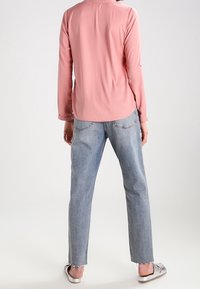 Haut rose clair à manches longues avec un ourlet arrondi, associé à un jean bleu clair à jambes droites. Tongs argentées avec une finition texturée.