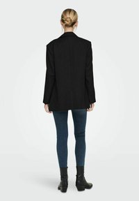 Blazer nero con un design su misura, maniche lunghe e taglio dritto. Indossato sopra jeans blu e stivali neri alla caviglia, con dettagli minimi.