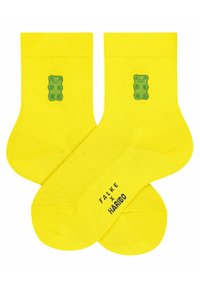 Gelbe Baumwollsocken mit einem grünen Gummibärchen-Motiv an der Seite und einem bedruckten "FALKE x HARIBO"-Label auf der Unterseite.