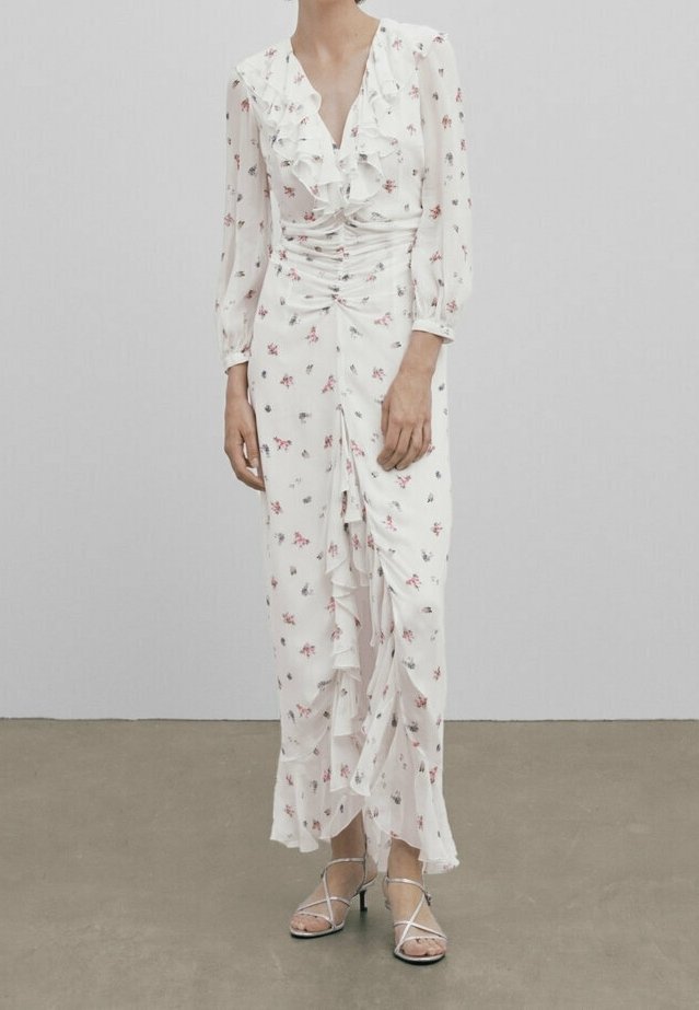 Robe blanche à manches longues avec un col froncé et un motif floral. Présente des détails froncés et une silhouette fluide. Accompagnée de talons à lanières.