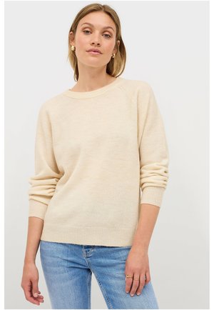 Lichtbeige gebreide trui met een relaxte pasvorm, geribde manchetten en zoom, en een ronde halslijn. Draagt met blauwe denim jeans.