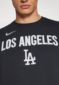 Melns kokvilnas t-krekls ar apaļu kaklu, ar baltu izšūtu tekstu "LOS ANGELES" un "LA" logo priekšpusē. Nike logo baltā krāsā.