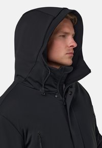 Černá nepromokavá bunda s vysokým límcem, nastavitelnou kapucí, zipovými kapsami a elegantní hladkou texturou. Vyznačuje se minimalistickým designem.