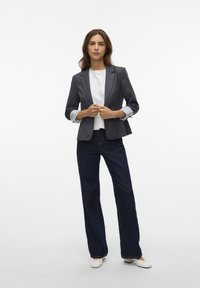 Dark gray blazer with notched lapels and rolled-up white striped sleeves, paired with wide-leg dark denim jeans and light-colored flats.