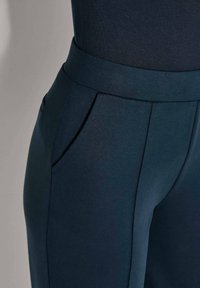 Close-up van donkerblauwe high-waisted broek met een brede tailleband, zijzakken en een voornaaddetail.