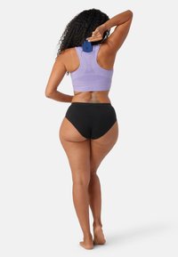 Lila atletisk crop top med mjuk ribbad textur, kombinerad med svarta högmidjade underkläder. En smartphone är delvis instoppad i toppen.
