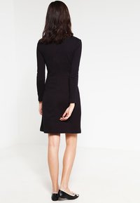 Svart långärmad klänning med en åtsittande silhuett, längd till mitten av låret och en ren design. Kommer tillsammans med svarta flatskor med vita accenter.