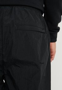 Svart nylonbyxor med kropplig textur, elastisk midjeband och en enda bakficka för förvaring. Enkelt och funktionellt design.