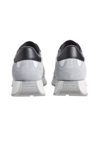 Zapatillas gris y blancas con parte superior de ante y cuero, cuello acolchado y suela de goma texturizada. Presenta el logotipo de la marca en el talón.