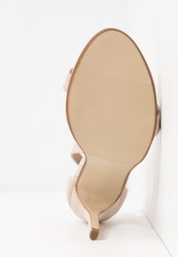 Chaussure à talons aiguilles nude avec un bout pointu et un fin talon aiguille ; dessus en cuir lisse et semelle en caoutchouc texturé.