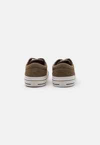Brune semskede lavtop sneakers med hvite gummisåler, med polstret krage og minimalistisk design. Ingen distinkte mønstre eller detaljer.