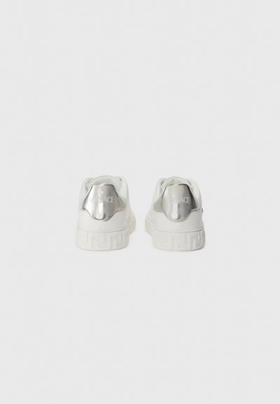 White sneakers with a glossy silver heel accent. Features embossed logo and patterned sole. Smooth material, rounded design, minimalistic style.