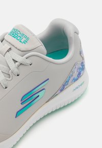 Jasnoszare sneakersy z gładką, syntetyczną cholewką, akcentami w kolorze teal, kwiatowym zdobieniem na pięcie oraz teksturowaną białą podeszwą.