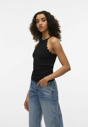Top de tirantes negro, texturizado, con escote festoneado, diseño ajustado, combinado con unos jeans sueltos de color azul claro. El modelo está de perfil.