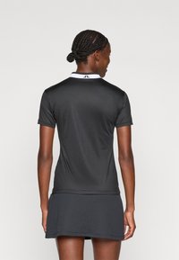 Camisa polo atl�ética preta com colarinho branco, mangas curtas e saia plissada. Textura suave com detalhes mínimos.