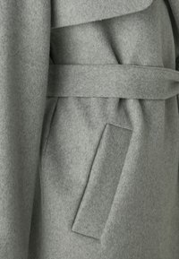 Grey felt coat with a wide collar, belt, and side pocket. The fabric features a soft, textured weave for warmth and comfort.