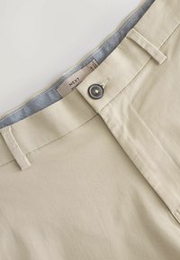 Beige Hosen mit einem Knopfverschluss, Gürtelschlaufen und einem kontrastierenden blauen Karolining. Glatte Textur mit schmaler Passform.