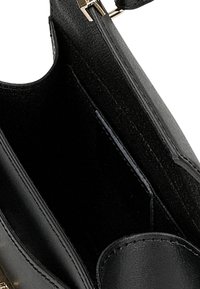 Intérieur d'un sac à main en cuir noir, présentant une texture lisse, un seul compartiment et une petite poche plate sur un côté, avec des accessoires en or.