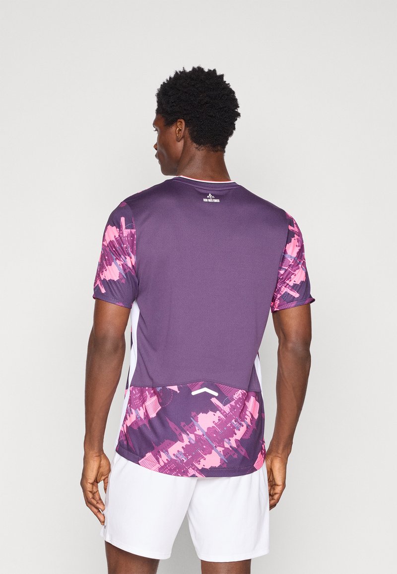 Maglietta sportiva viola con motivo astratto rosa sulle maniche e sul bordo inferiore; maniche corte, collo rotondo e tessuto leggero.