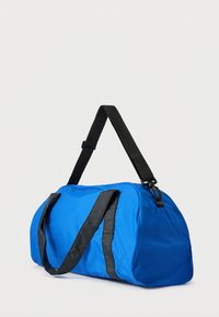 Μπλε σακ βουαγιάζ κατασκευασμένο από υφασμάτινη υφή με μαύρες ιμάντες, διαθέτει κυρτό σχήμα και πλαϊνή τσέπη για επιπλέον αποθηκευτικό χώρο.