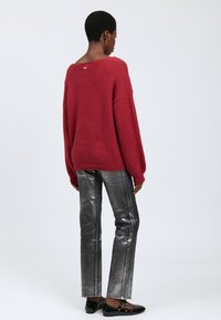 Maglione rosso peloso con scollo ampio, abbinato a pantaloni dritti argentati lucidi con strisce laterali e ballerine nere.