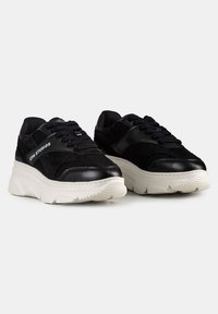 Baskets noires à la texture en maille et cuir lisse. Semelle blanche épaisse avec un motif de crampons subtil. Fermeture à lacets avec un détail de marque.