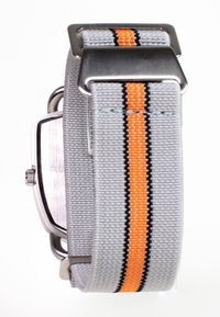 Grå vævet stofurrem med orange og sorte striber, rustfrit stål hardware og en kvadratisk bagside, der er synlig til venstre.