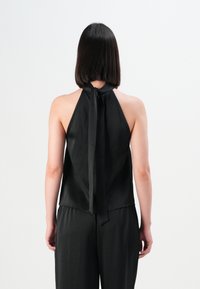 Sort halterneck top med bindebånd, der har en glat tekstur og løst fit, båret over matchende sorte bukser med elastisk talje.