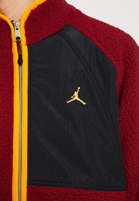 Rote Fleecejacke mit schwarzem Einsatz und gelben Reißverschlussakzenten; mit gesticktem Jumpman-Logo in Gelb auf dem schwarzen Bereich.