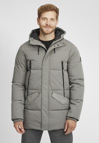 Doudoune grise à capuche, avec une fermeture à glissière, deux poches avant et des zippers sur les côtés, rehaussée de finitions et de matériaux noirs.