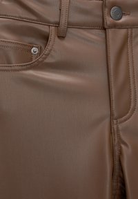 Hnědé kožené kalhoty zblízka, ukazující přední kapsu, poutko na opasek, šití a detaily kovového knoflíku.