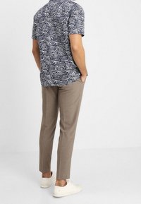 Camicia a manica corta con un motivo a onde blu e bianche; abbinata a pantaloni beige chiaro su misura e sneakers bianche.