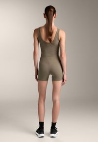 Olivno zeleno prilegajoče bodysuit z rebrasto teksturo, brez rokavov in nizkim hrbtom. V kombinaciji z črnimi nogavicami do gležnjev in športnimi čevlji.