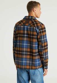 Gestructureerde flanellen shirt in blauw, bruin en zwart met een knoop-down kraag, met contrasterende texturen en een leren accent op de achterkant.
