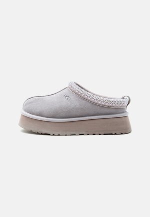 Svetlosivá slip-on obuv UGG s hrubou béžovou podrážkou, prešitým lemom okolo otvoru a logom UGG na boku, zobrazená z vnútornej strany.