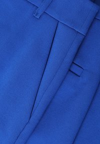 Niebieska tkanina ukazująca dopasowane spodnie, charakteryzująca się gładką fakturą, prostym krojem i subtelnym detalem plisowania. Perspektywa zbliżenia.