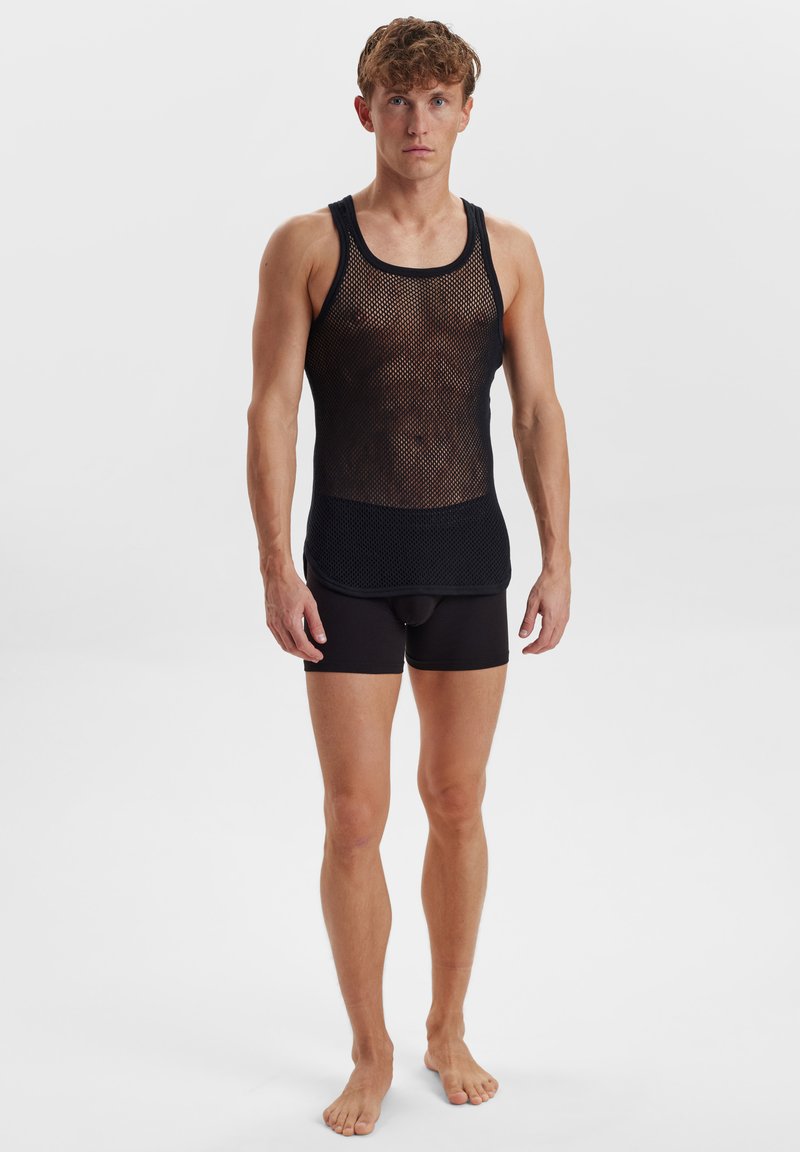 Sort mesh tank top med rund halsudskæring, prydet med et struktureret mønster, parret med sorte tætsiddende shorts. Enkel, moderne atletisk design.