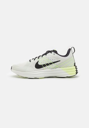 Chaussure de course Nike blanche et vert néon avec logo swoosh noir, lacets noirs et semelle Lunar coussinée, vue latérale sur fond uni.