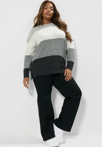 Sweter dziany w poziome paski w kolorze białym, szarym i czarnym; połączony z czarnymi spodniami i białymi trampkami. Miękka tekstura, luźny krój.