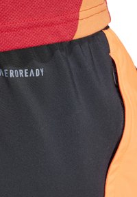 Zwarte sportshorts met oranje accenten, voorzien van een gestructureerde tailleband met het label "AEROREADY." Het materiaal lijkt glad en vochtregulerend.