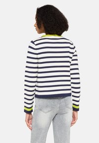 Sweter w paski w kolorze granatowym i białym, z fakturowanej tkaniny, krótki fason, zielony kołnierz i mankiety, długie rękawy, noszony z jasnoszarymi dżinsami.